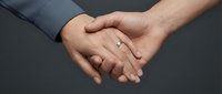 Two people joining hands together in a gesture of unity, teamwork, and partnership against a neutral gray background for corporate and business concepts.