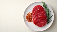 Raw beef ribeye steaks with fresh rosemary and red lentils on white plate against neutral background, ready for cooking.