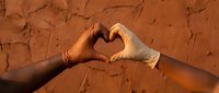 Two hands forming heart shape against cracked dry earth background symbolizing love, unity and environmental awareness in warm golden light.
