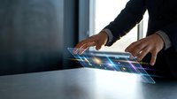 Businessman in dark suit touching holographic digital interface with glowing blue data visualization on table for technology, innovation, and business solutions.