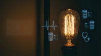Vintage Edison bulb glowing with warm filament against dark background with medical heartbeat monitor display creating healthcare technology concept.