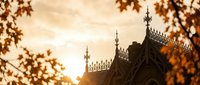 Gothic cathedral spires silhouetted against golden sunset sky with autumn foliage framing architectural details for religious and travel content.