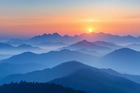 Majestic mountain ranges silhouetted against vibrant sunset sky, layered peaks fade into misty blue haze creating atmospheric perspective, golden sun setting behind ridges.