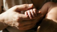 Newborn baby hand gently gripping adult fingers in a warm, tender moment of parental love and family bonding.