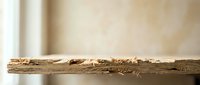 Termite damaged wooden plank with sawdust debris on surface showing pest infestation destruction in home interior.