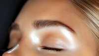 Close-up view of professionally done eye makeup with shimmering white eyeshadow and perfectly shaped eyebrow on tanned skin. Demonstrates beauty and cosmetic application.