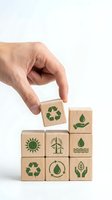 Hand placing wooden cube with recycling symbol on stack of eco-friendly blocks featuring green energy icons on white background for sustainability concepts.