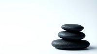 Stacked smooth dark stones arranged in pyramid formation on white background, symbolizing balance, wellness, and meditation for spa and relaxation concepts.
