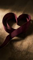 Burgundy ribbon forming heart shape on textured burlap fabric with warm lighting for romantic crafts and Valentine decorations.