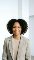 Professional African American businesswoman with curly hair smiling confidently in modern office wearing beige blazer and sweater for corporate headshot.