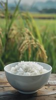 Bowl of cooked white rice on wooden table with rice field background showcasing farm to table concept for healthy eating and Asian cuisine preparation.
