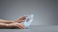 Female hand holding transparent glass water bottle against neutral gray background, suitable for beverage, hydration, wellness, and product marketing campaigns.