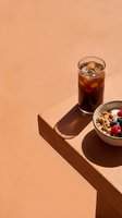 Cold cola beverage with ice cubes and granola cereal bowl with fresh berries on beige table for breakfast or brunch advertising.