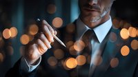 Businessman in formal suit holding pen against dark background with golden bokeh lights, creating atmosphere of success and decision-making.