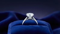 Classic solitaire diamond engagement ring in elegant blue velvet jewelry box with dramatic lighting and silk fabric background for luxury proposals.