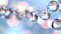 Transparent water droplets or bubbles floating in air with soft blue and pink bokeh background creating dreamy atmosphere.