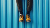 Person in black leather pants and brown boots hanging legs against blue striped wall background for fashion and lifestyle concepts.
