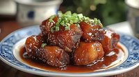 Glazed pork belly chunks in dark soy sauce with green onion garnish served on traditional blue and white porcelain plate, close up view of Asian cuisine.