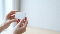 Woman with medium skin tone holding blank white business card or gift card in both hands, suitable for branding, corporate identity, and marketing mockup projects.