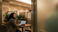 Professional businesswoman working on laptop in modern office cafe environment with warm lighting and contemporary interior design.
