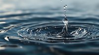 Single water drop splashing on dark blue water surface creating crown splash formation with multiple droplets and concentric ripple patterns in macro photography.