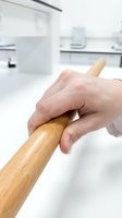 Hand holding wooden rolling pin in modern white kitchen ready for baking and cooking preparation.