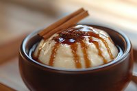 Creamy vanilla pudding topped with caramel sauce and cinnamon powder in rustic brown ceramic bowl, close-up view with selective focus on dessert surface.