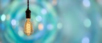 Vintage Edison bulb hanging against soft turquoise bokeh background with warm glowing filament creating cozy atmospheric lighting for interior design concepts.