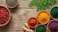 Colorful superfood powders and seeds in wooden bowls on rustic table with fresh moringa leaves for healthy nutrition and wellness lifestyle.
