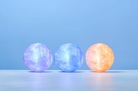 Glowing spherical lamps in purple, blue and orange colors arranged in row on light surface against blue background create modern minimalist composition.