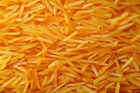 Raw yellow rice grains in macro view showing detailed texture and natural pattern of uncooked basmati rice scattered across frame, suitable for food industry and packaging.
