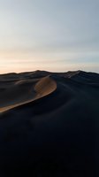 Dramatic sand dunes at golden hour with soft shadows and warm light creating stunning desert landscape for travel and nature backgrounds.