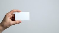 Male hand holding blank white business card against neutral gray background, suitable for branding, corporate identity, and marketing mockup designs.