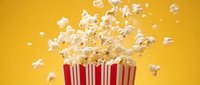 Fresh popcorn exploding from red striped container against bright yellow background. Cinema snack food concept for entertainment and movie themes.