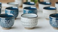 Handcrafted ceramic bowls with intricate patterns in blue and white glazes arranged in rows, featuring traditional designs and natural clay bases. For home decor and tableware.