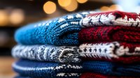 Cozy knitted winter sweaters in blue, red and gray colors stacked neatly with festive bokeh lights background, seasonal fashion and warmth concept.