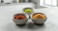 Three white ceramic bowls filled with colorful spices and herbs arranged on modern kitchen counter for culinary cooking and food preparation.