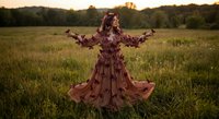 Young woman in flowing floral dress with arms outstretched in golden hour meadow, expressing freedom and connection with nature during sunset.