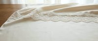 Cream linen fabric with delicate lace trim detail, isolated on wooden surface for textile, fashion design, and home decor projects.