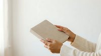 Close-up of hands holding a neutral linen clutch wallet against a white background, suitable for fashion, lifestyle, and product photography.