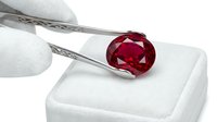 Faceted ruby gemstone held by tweezers over white display block for jewelry appraisal, gemology, and luxury retail purposes.