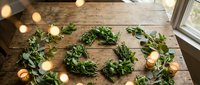 Fresh green eucalyptus garland with warm string lights on rustic wooden table creating cozy natural home decor atmosphere for holidays and celebrations.
