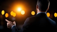 Businessman in dark suit pointing forward against blurred bokeh lights and bright sun glow, back view, leadership concept for business presentations.