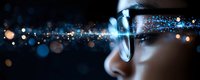 Close up profile view of person wearing glasses with glowing blue bokeh light effects and sparkles creating magical atmosphere against dark background.