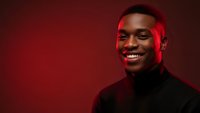 Young African American man smiling confidently in black turtleneck against red background with dramatic lighting for portrait photography.