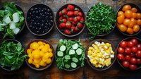 Fresh colorful ingredients in black bowls on rustic wooden table including strawberries, olives, tomatoes, microgreens, cucumber slices and diced cheese arranged in row.