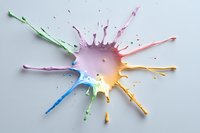 Colorful paint splash explosion in rainbow colors on light gray background, dynamic liquid art with splatter effect and drops creating abstract pattern.