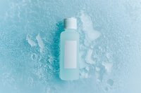 White cosmetic bottle on frozen turquoise background with ice crystals and frost patterns creating minimalist winter skincare composition.