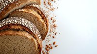 Fresh sliced whole grain bread with scattered seeds and crumbs on white background, artisanal bakery product photographed from above for food marketing.