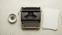 Vintage black typewriter on white desk with blank paper sheets and paper clips, flat lay top view for creative writing concept.